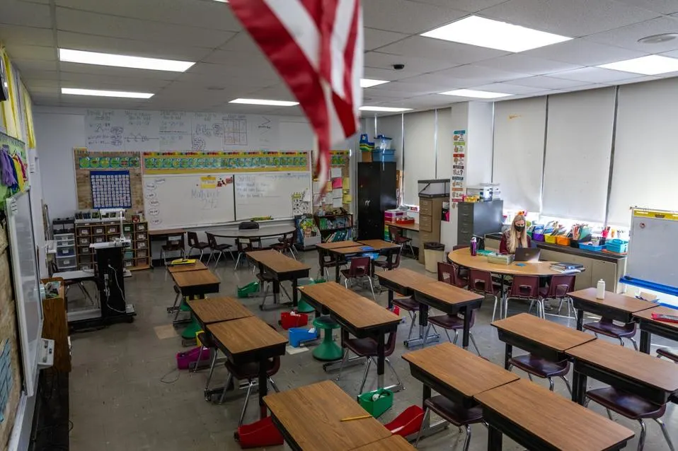 Teacher in empty school classroom with American flag.