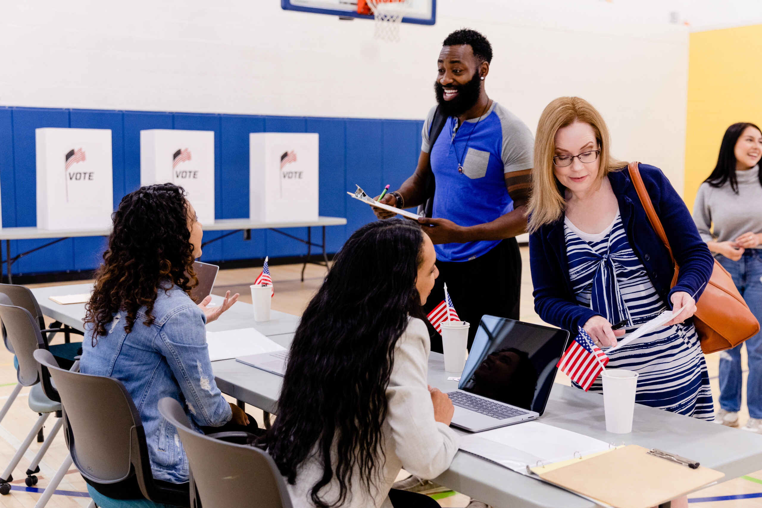 The female election volunteers sit at the table and greet voters to the community center.