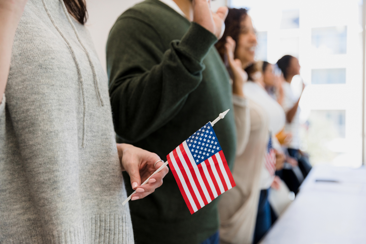 The group of multiracial people stand and raise their hand to say the pledge.